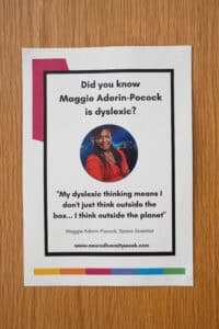 A poster on a wooden surface features Maggie Aderin-Pocock and reads: “Did you know Maggie Aderin-Pocock is dyslexic? ‘My dyslexic thinking means I don’t just think outside the box… I think outside the planet.’” Celebrate neurodiversity awareness.