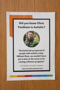 A poster on a wooden surface reads: Did you know Chris Packham is Autistic? with his photo. Below, a quotation highlights the value of autistic traits in achievement. Celebrate Neurodiversity this Neurodiversity Celebration Week at neurodiversityweek.com.